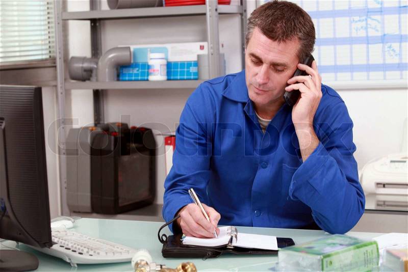 Plumber taking a call in an office and making an appointment in his diary, stock photo