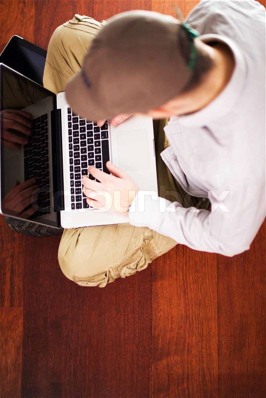 Guy with Laptop Seating on the Dark Brown Hardwood Floor. Computers Photo Collection, stock photo