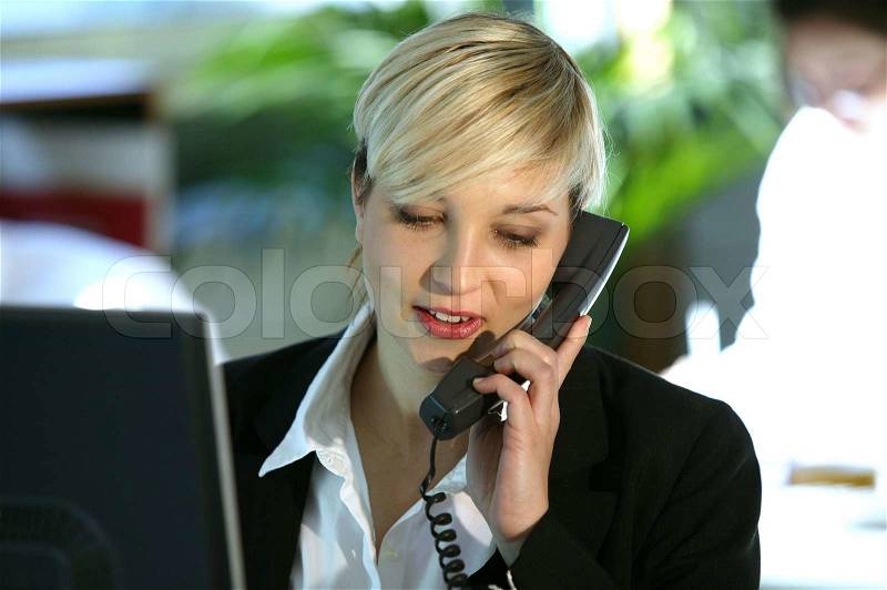 Blond office worker using land-line telephone, stock photo