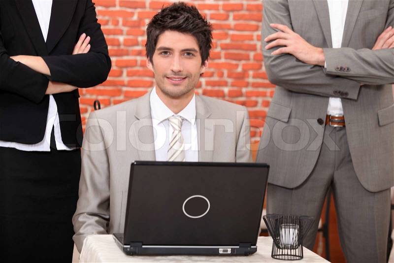 Man using a laptop flanked by people in suits, stock photo