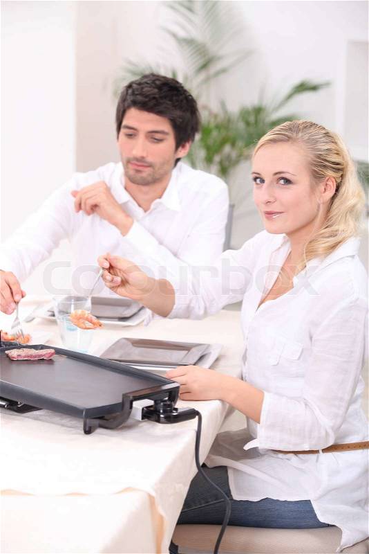 Couple cooking meat on a tabletop electric plate, stock photo