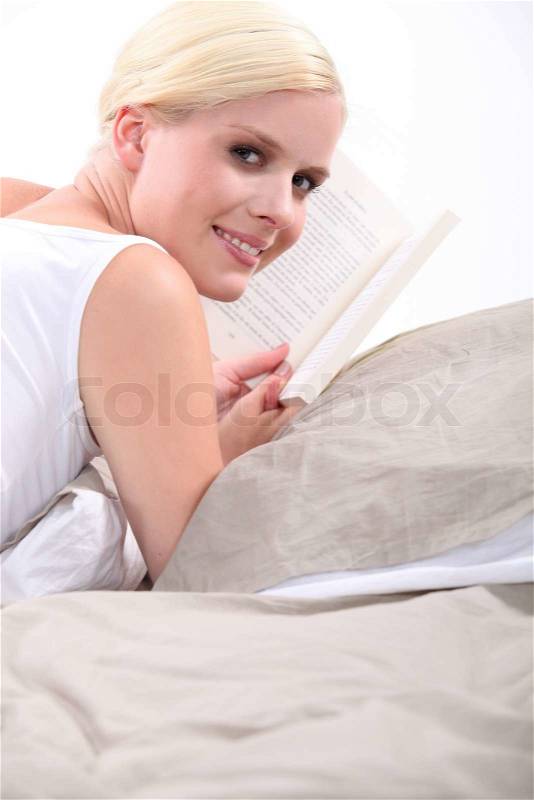 Young blond woman reading a book on her bed, stock photo
