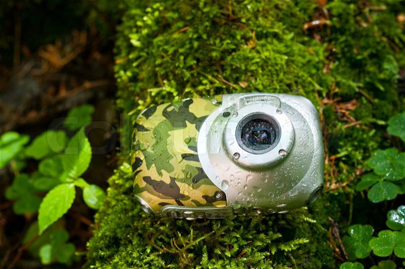 Waterproof compact camera covered with water drops lying on the forest floor, stock photo