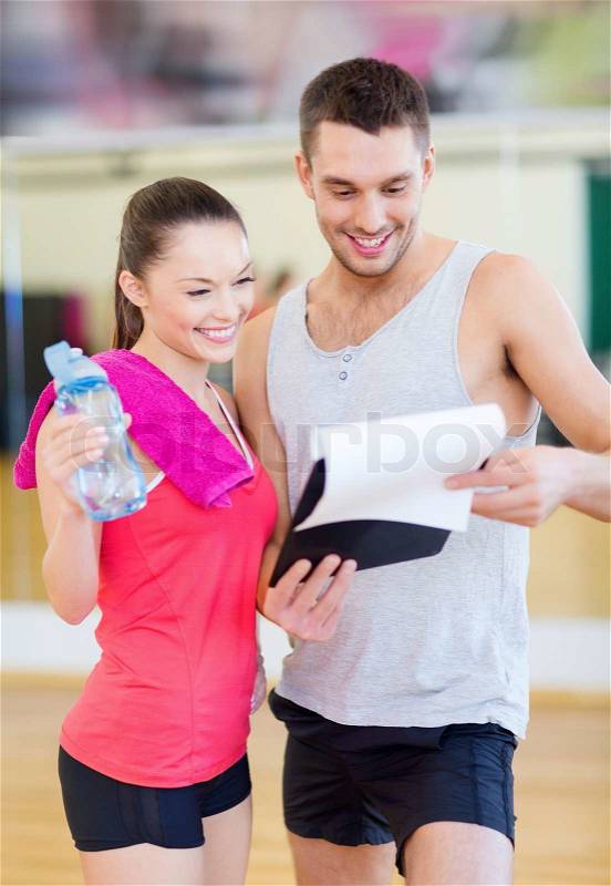 Fitness, sport, training, gym and lifestyle concept - smiling male trainer with clipboard and woman with water bottle in the gym, stock photo