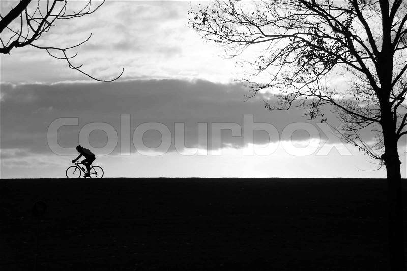 Solitary biker in silhouette is biking at the countryside at sunset in black and white, stock photo