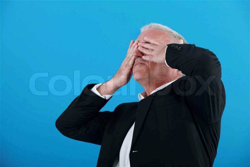 Senior businessman covering his eyes with his hands, stock photo