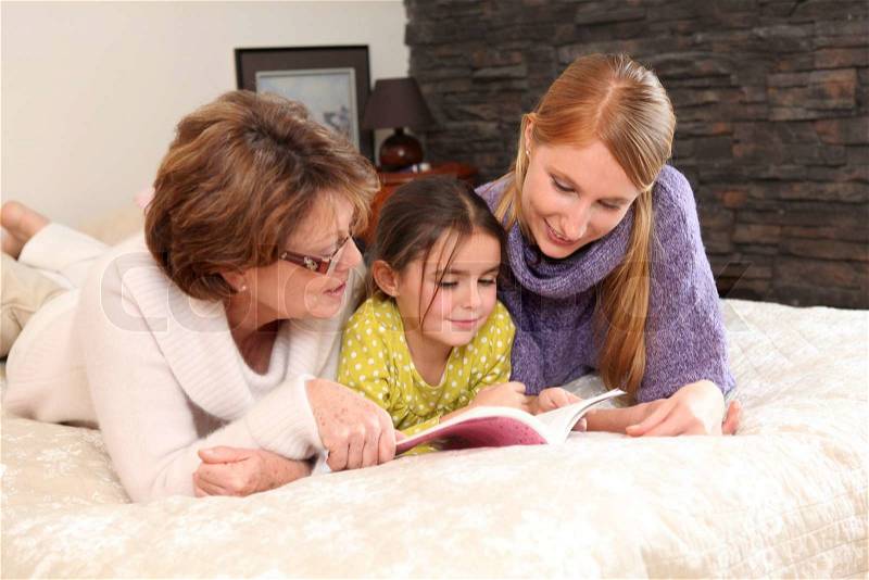 Mother and grandma reading with little girl, stock photo