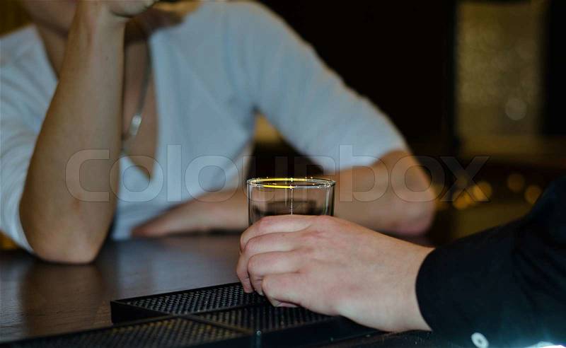 Close up of a male hand holding a glass tumbler on a bar counter as he sits drinking with a friend, stock photo