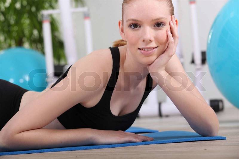 Young woman lying on a gym mat, stock photo