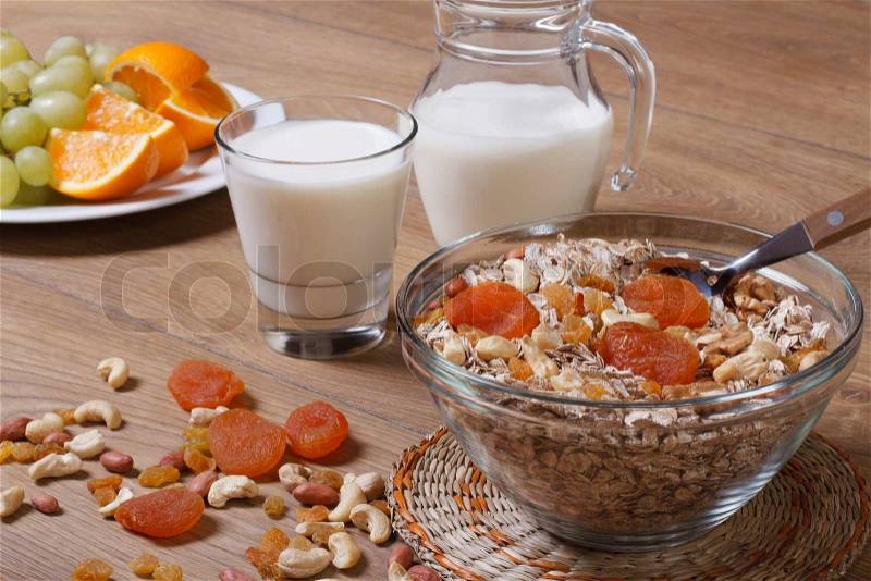 Flakes with raisins, nuts and dried apricots and milk. Fresh fruit in the background, stock photo