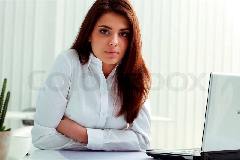 Young serious businesswoman sitting at the table in office, stock photo