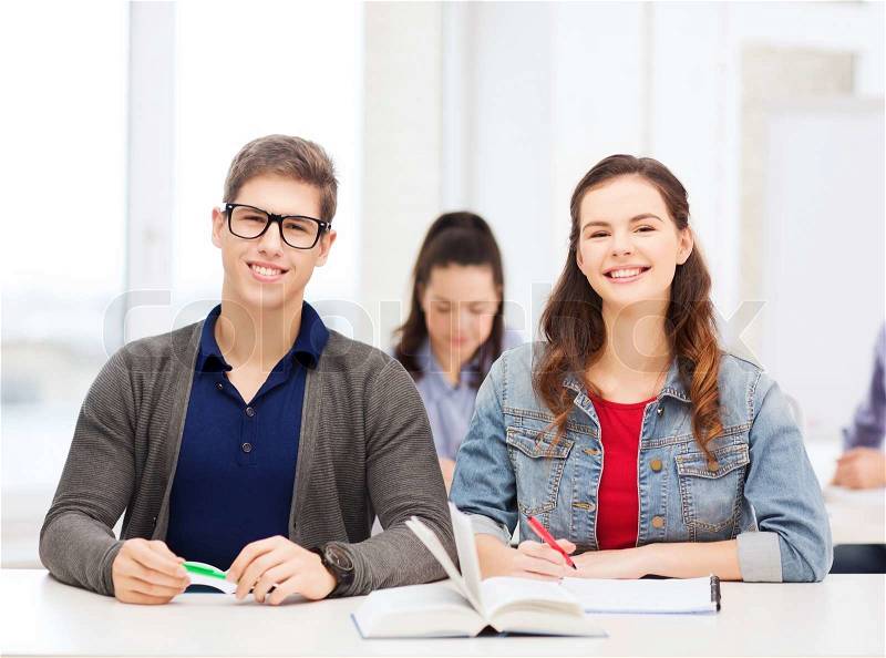 Education, school and people concept - two teenagers with notebooks and book at school, stock photo