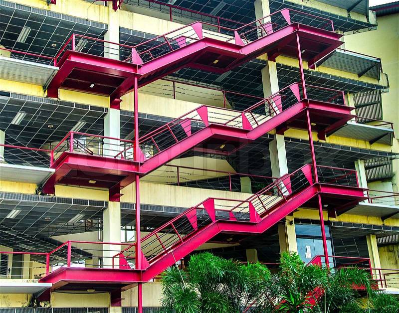 Red metal staircase going up the side of building on the outside, stock photo