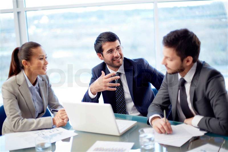 Portrait of three co-workers discussing business plan in office, stock photo