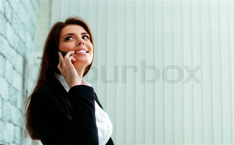 Young happy businesswoman talking on the phone and looking away at copyspace in office, stock photo