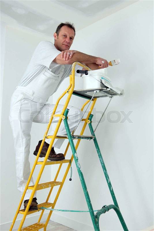 Painter climbing ladder to paint ceiling, stock photo