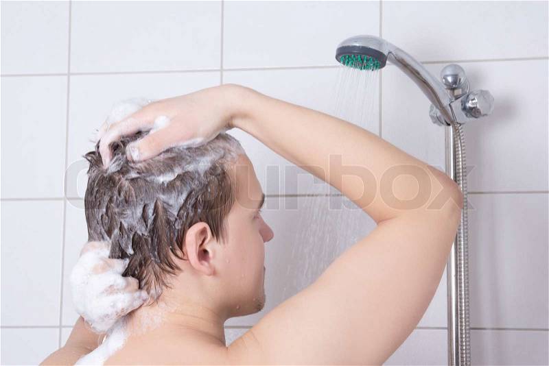 Back view of young attractive man washing hair in shower, stock photo