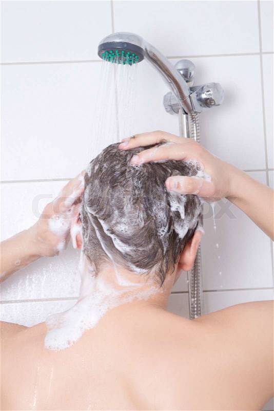 Back view of young attractive man washing hair with shampoo in shower, stock photo