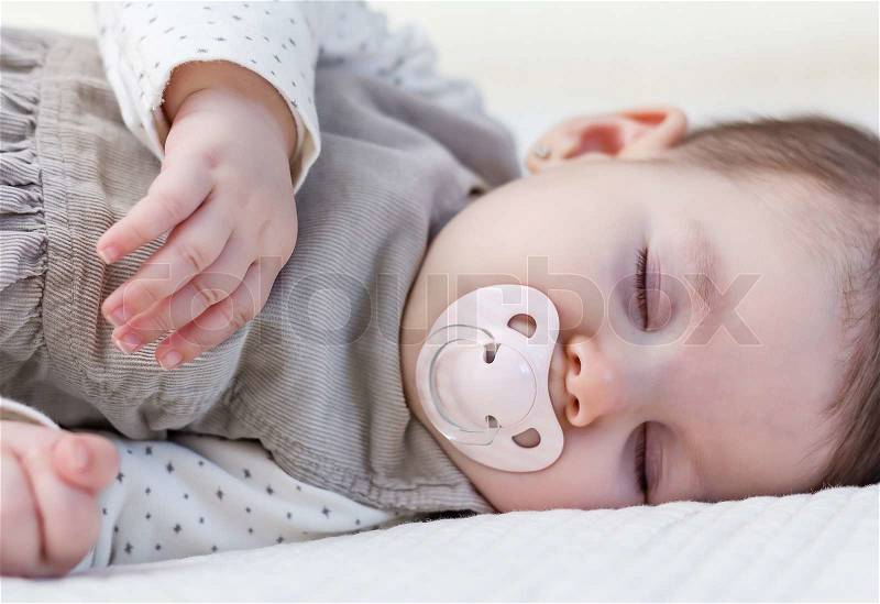 Cute baby girl with pacifier sleeping over white bedcover, stock photo