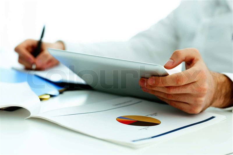 Closeup image of a man holding tablet computer and writing something down, stock photo