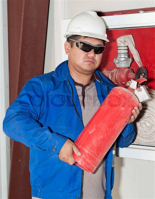 The worker in a uniform moves the big fire extinguisher on a production site, stock photo