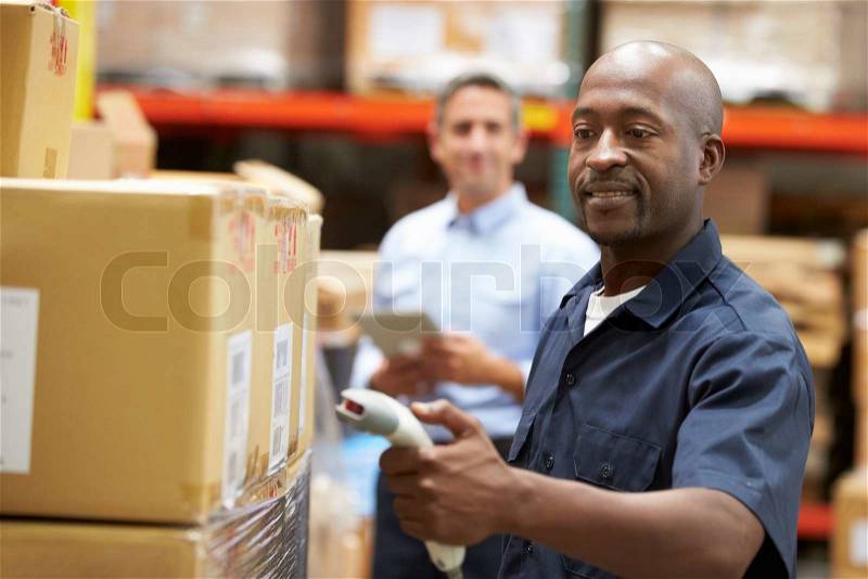 Manager In Warehouse With Worker Scanning Box In Foreground, stock photo