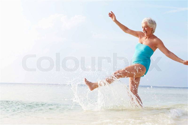 Senior Woman Splashing In Sea On Beach Holiday, stock photo