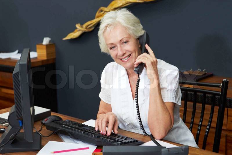 Hotel Receptionist Using Computer And Phone, stock photo