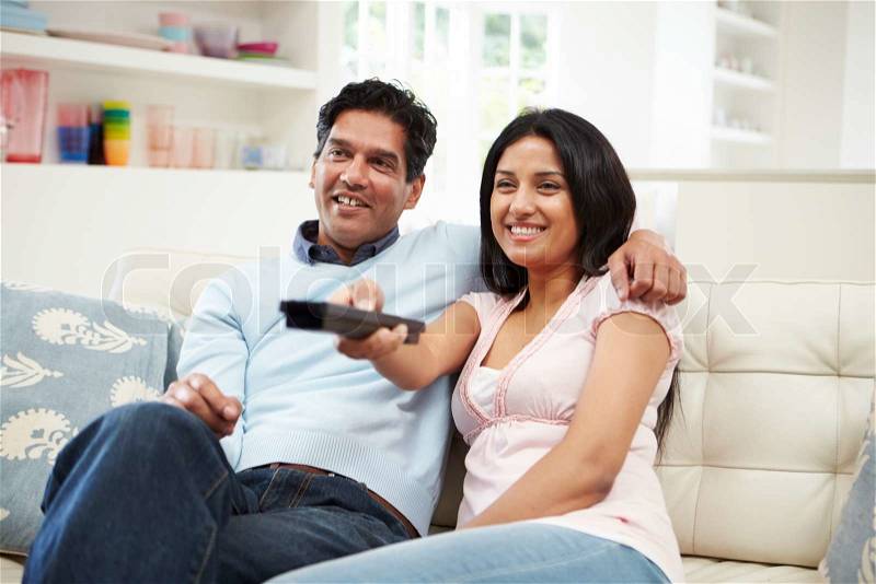 Indian Couple Sitting On Sofa Watching TV Together, stock photo