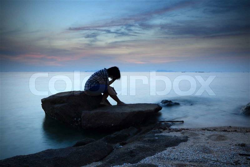 Woman sitting and contemplating alon on the rock by the beach, stock photo