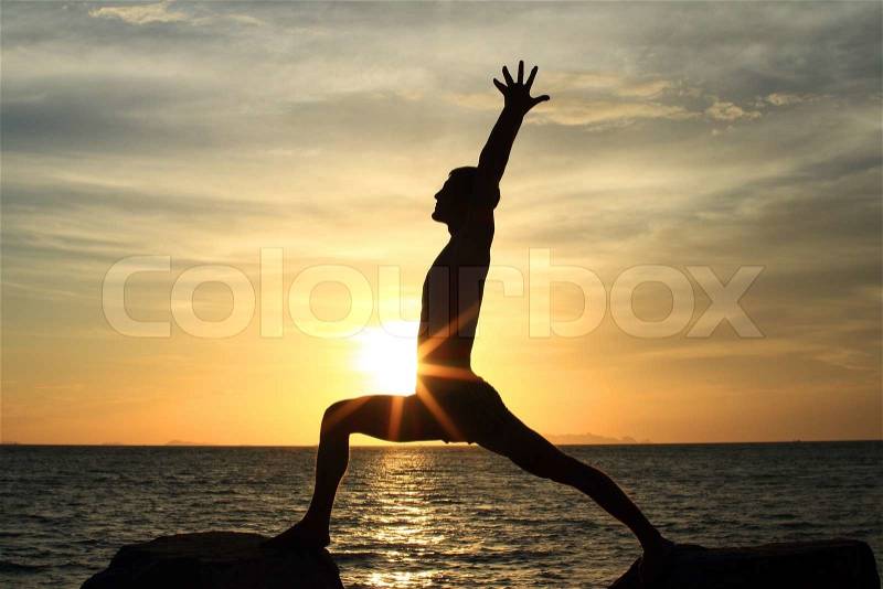 Silhouette of perfect body man acts yoga on the rock with sea sunet background, stock photo