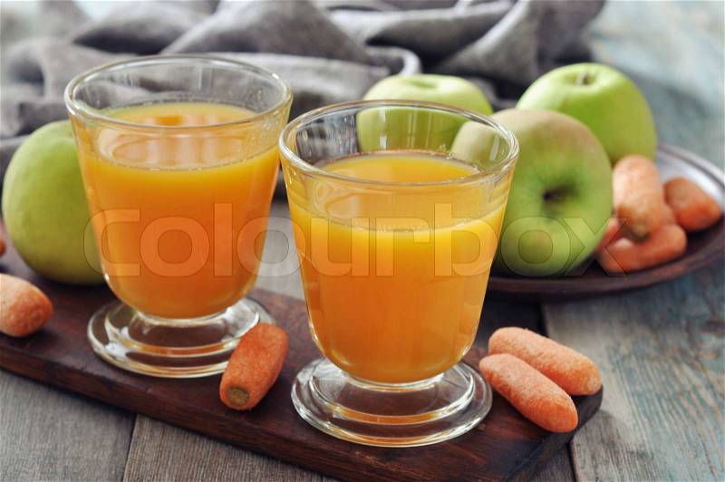 Apple and carrot juice in glass with fresh vegetables and fruits on wooden background, stock photo