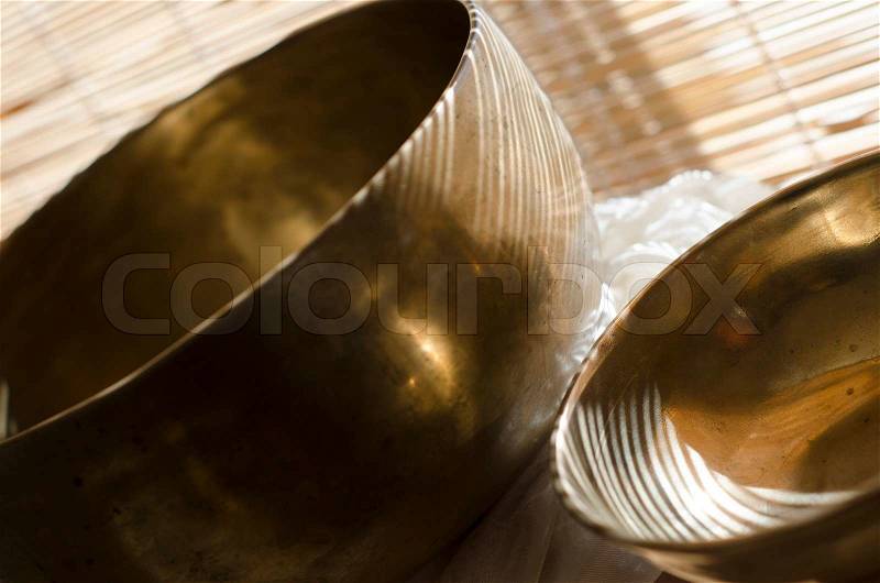 One large and one smaller Tibetan singing bowls on a table in sunlight, stock photo