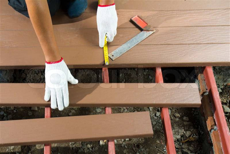 Worker installing wood floor for patio, stock photo