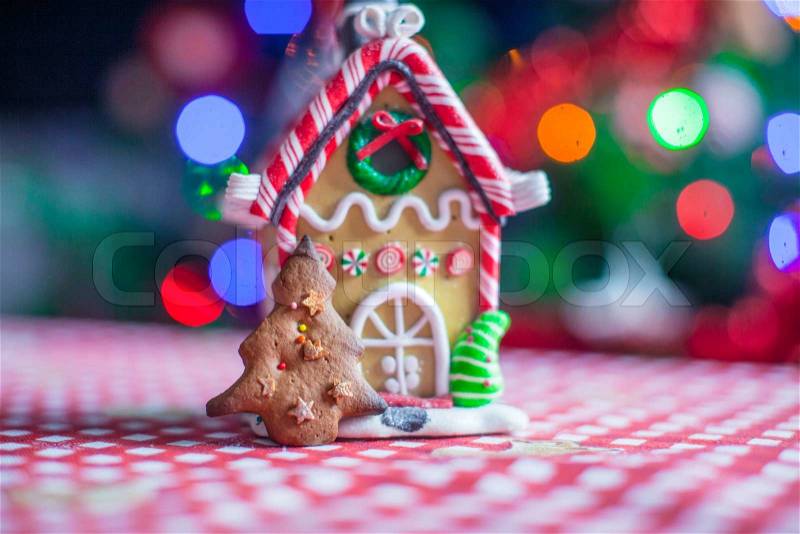 Gingerbread house decorated by sweet candies on a background of bright Christmas tree with garland, stock photo
