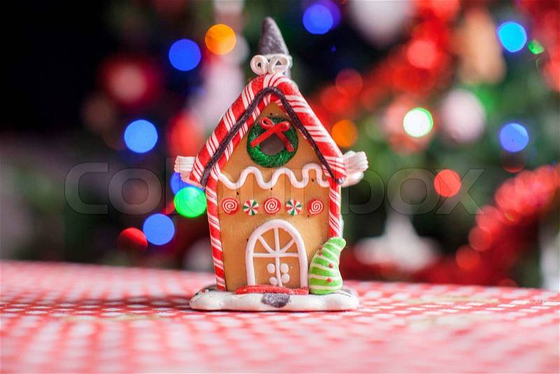 Gingerbread house decorated by sweet candies on a background of bright Christmas tree with garland, stock photo