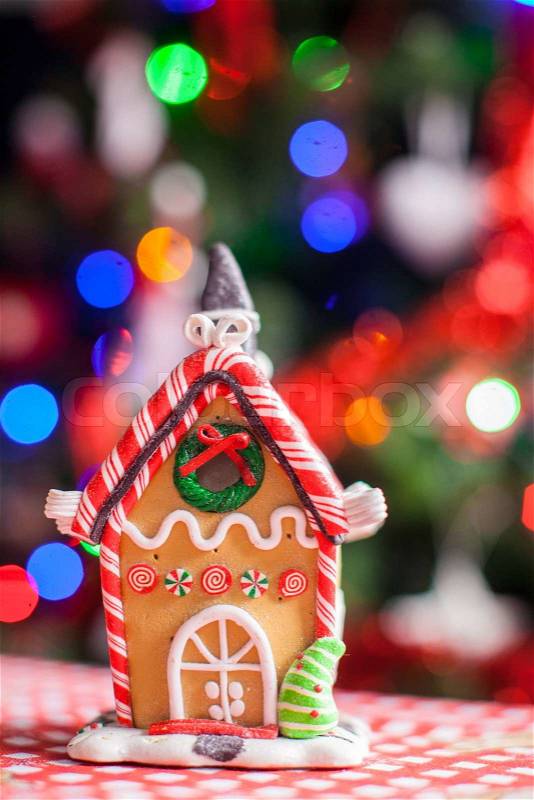 Gingerbread fairy house decorated with colorful candies on a background of bright Christmas tree with garland, stock photo