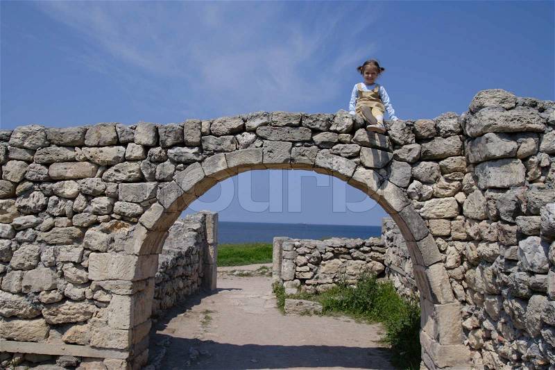 Little child sitting on a stone arch with blue cloudy sky at the background. Crimea. Ukraine. , stock photo