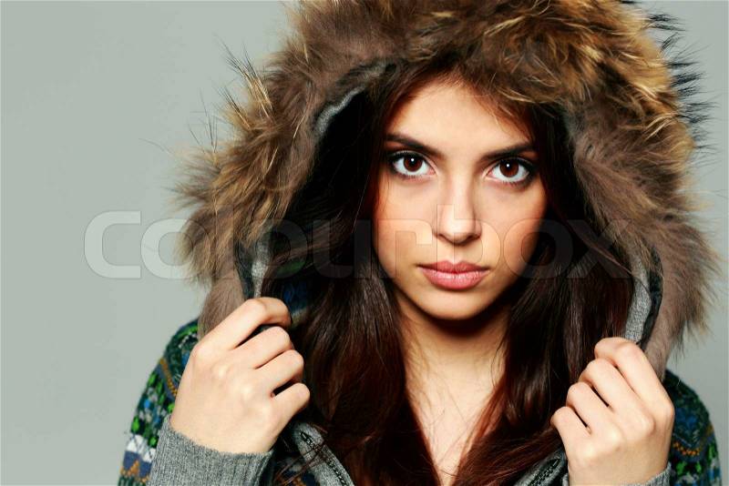 Closeup portrait of a young pensive woman in warm winter outfit on gray background, stock photo