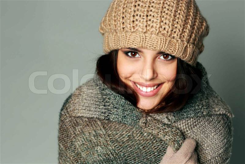 Closeup portrait of a young happy woman in warm winter outfit on gray background, stock photo