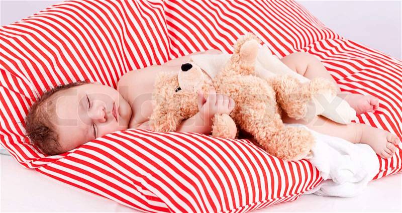 Sleeping cute little baby on red and white stripes pillow with teddy bear, stock photo