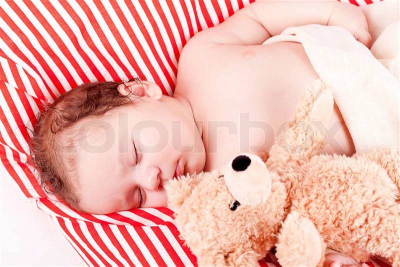 Sleeping cute little baby on red and white stripes pillow with teddy bear, stock photo
