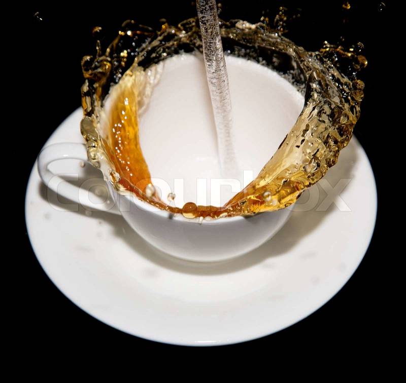 Tea being poured into a saucer with splashes on a black background, stock photo
