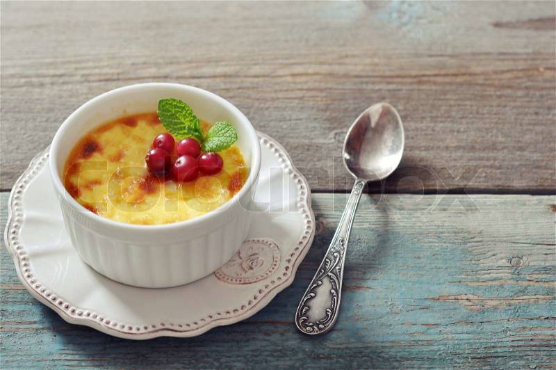 The creme brulee in ceramic baking mold with mint and berries on wooden table, stock photo