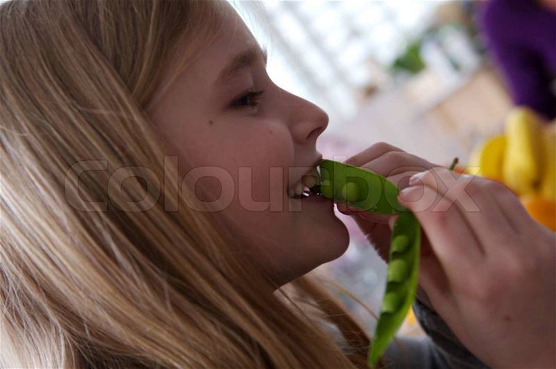 A happy caucasian girl eating fresh peas, stock photo