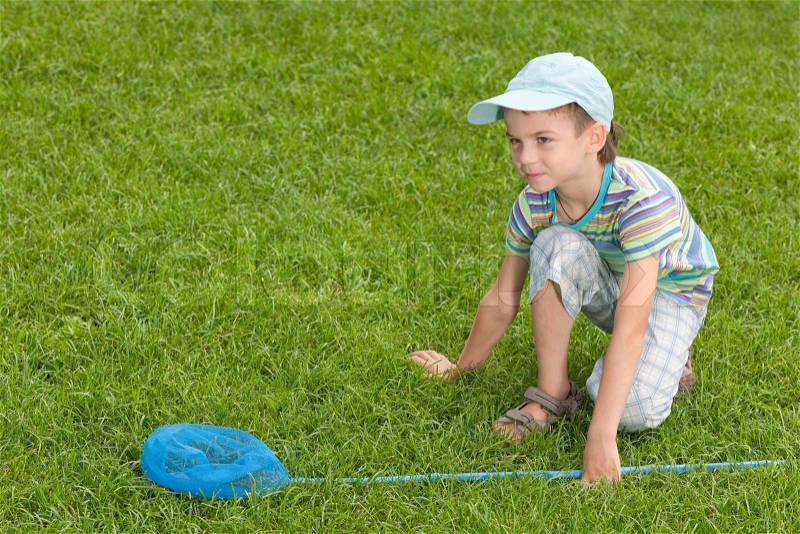 A boy with a butterfly net is sitting on the summer lawn , stock photo