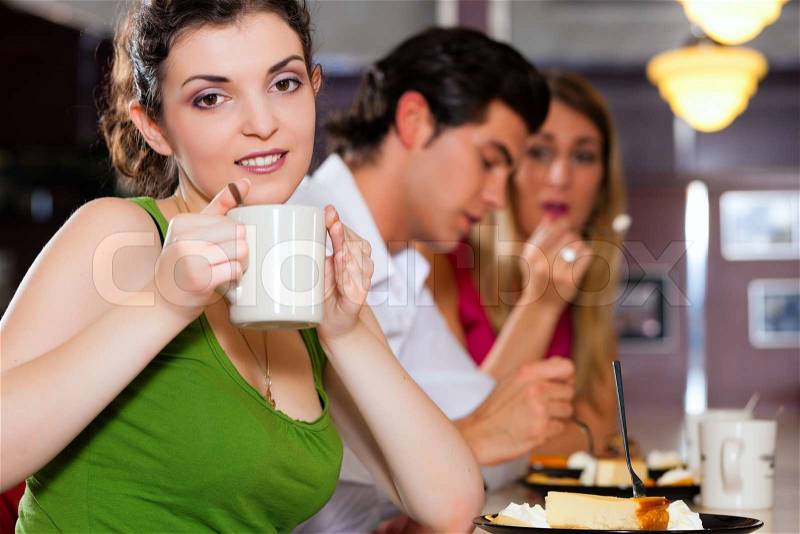 Three friends in a restaurant or diner eating cheesecake and drinking coffee, stock photo