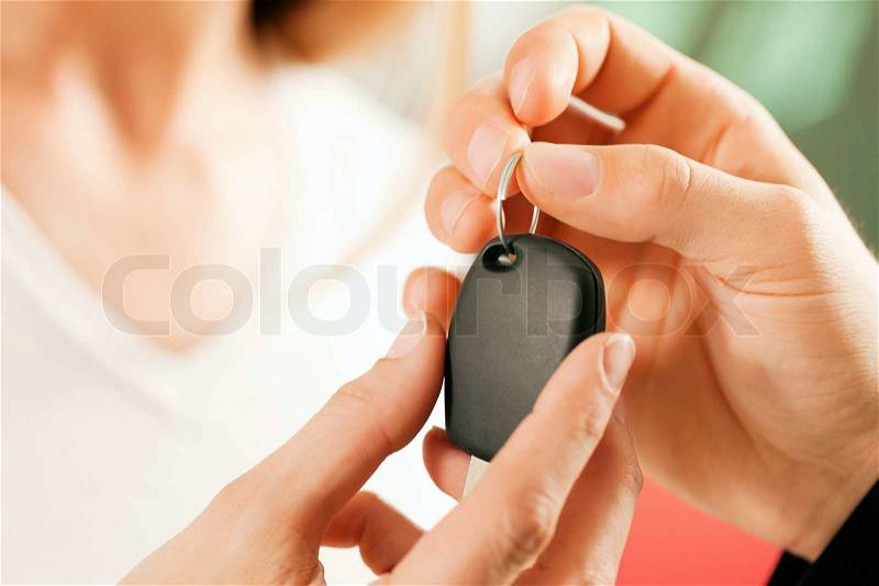 Woman at a car dealership buying an auto, the sales rep giving her the key, macro shot with focus on hands and key, stock photo