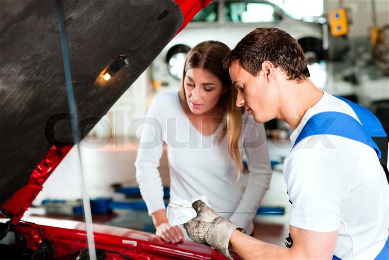 Woman talking to a car mechanic in his repair shop, both are standing next to the car, stock photo