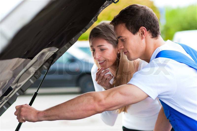 Woman talking to a car mechanic in a parking area, both are standing next to the car, stock photo